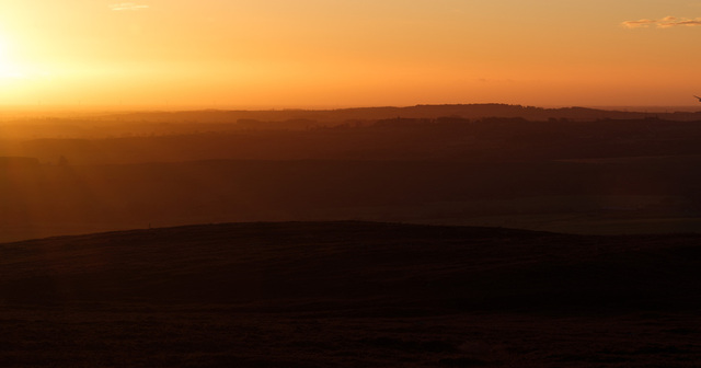 Right half of a sunrise diptych. The sun rises just above the horizon on the top left edge of the frame, casting layered shades of silhouetted hills in the morning haze.