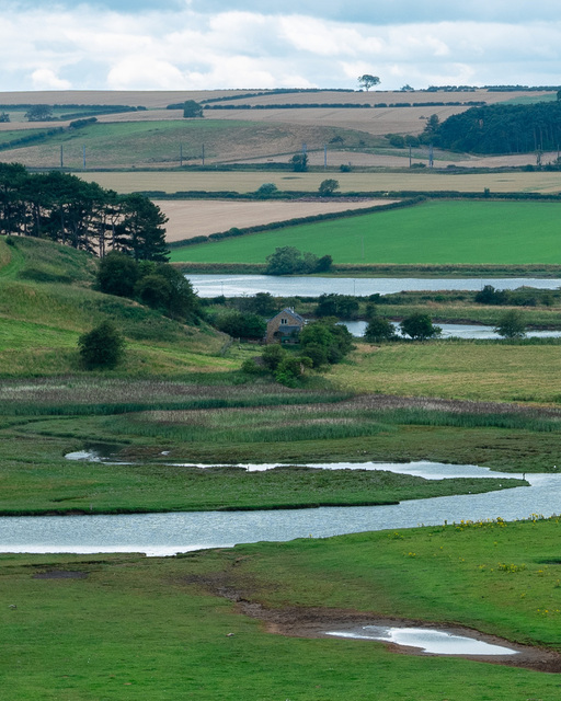 A cottage nestled amongst trees at the foot of a hill, on the banks of the river Aln
